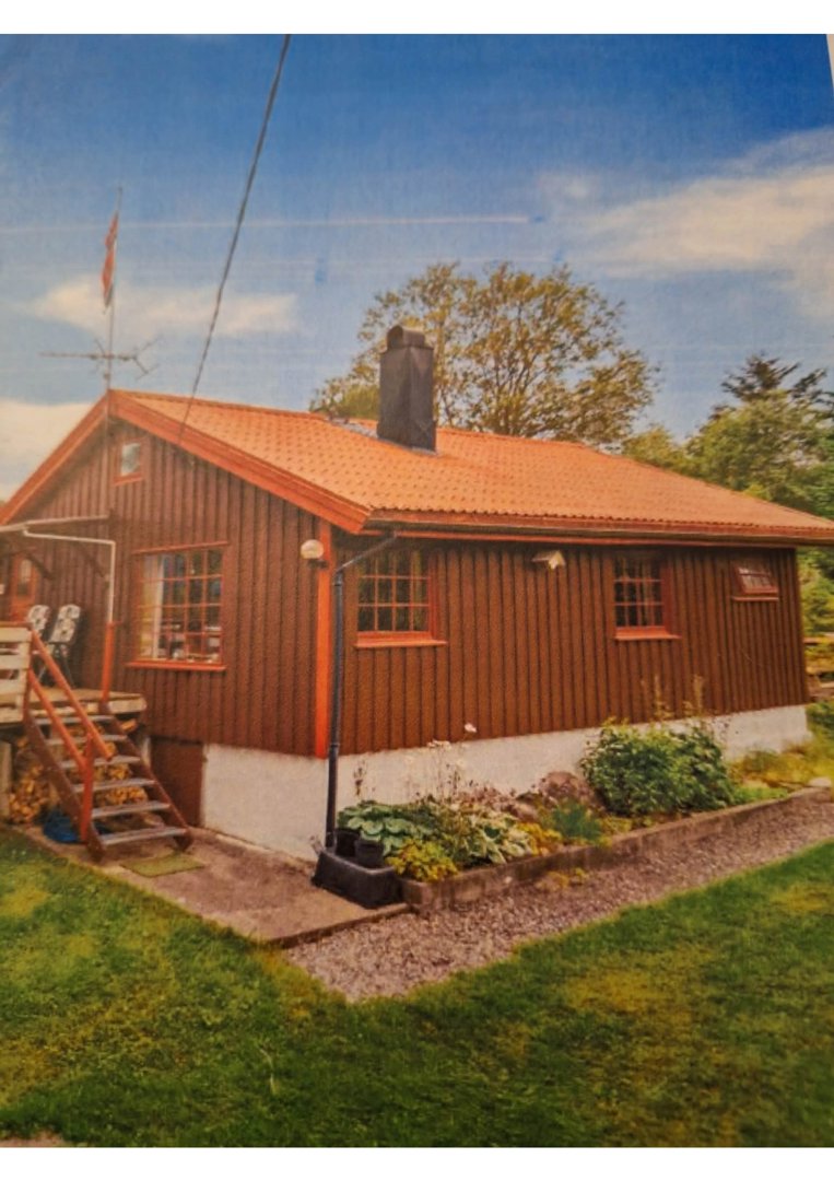 Fotografi av en eksisterende trehus med rødt tak og hage.