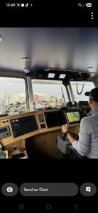 Fotografi av en person som sitter i et båtkommando (brønn) og styrer båten. Bildet viser interiøret med instrumentpaneler og utsikt over vannet.