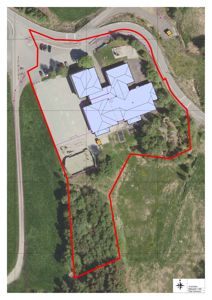 Situasjonsplan som viser en bygning på en tomt med omgivende terreng, veg og skog. Bygningen er markert med en rød linje.