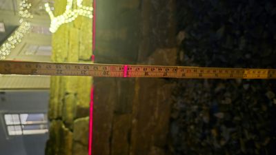 Fotografi av en steinmur med en målebånd og en rød laserlinje for måling.