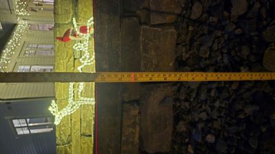 Fotografi av en bygning med julepynt, der en målebånd er plassert foran en steinvegg.