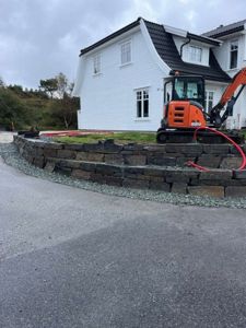 Fotografi av en nybygd hvit villa under anleggsarbeid, med en gressklipper og en steinmur i forgrunnen.