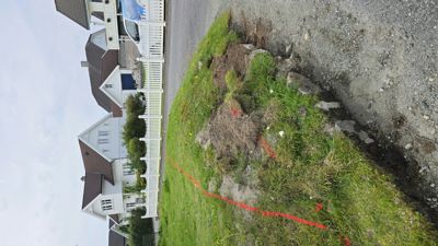 Fotografi av en tomt med grøfting og en rød markørstreng, med naboer i bakgrunnen.