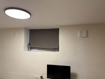 Fotografi av en vegg med et vindu, en taklampe og en TV.