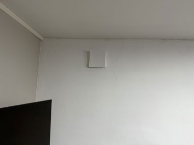 Fotografi av en hvit vegg i et rom, med en liten kvadratisk uttak i veggen og en del av en mørk TV-skjerm i forgrunnen.