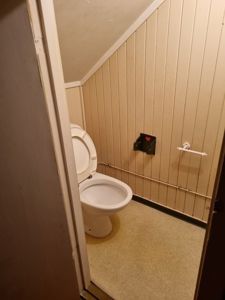 Fotografi av en toalettromsinnvendig med toalett, gulv og vegger med panel.