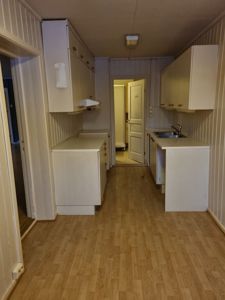 Fotografi av en kjøkkenrom med hvite skap, gulv og dører.