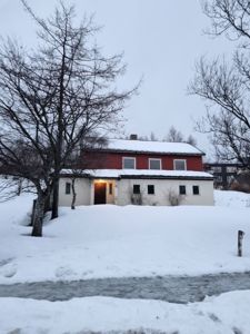 Fotografi av en toetasjes bolig med rød og hvit fasade, sett fra gaten i snø. Bildet viser eksisterende tilstand.