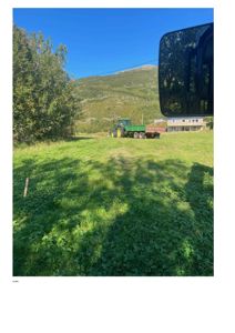 Fotografi av en grønn eng med en traktor og en bygning i bakgrunnen.