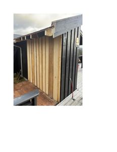 Fotografi av en bygning under oppføring eller ferdigstillelse, som viser fasadebehandling med både ubehandlet og svartfarget trepanel.