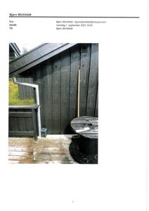 Fotografi av en mørk, trepanelert fasade på en bygning, sett fra et lite avstand. Bildet viser detaljer som en hvit nedløpsrør, en liten lysekrans, en gammel spole som benyttes som bord, og en delvis synlig terrasse. Bildet er inkludert i en e-post fra Bjørn Blichfeldt.