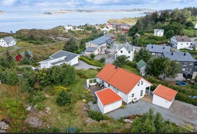 Luftfoto av en bolig med omgivelser, inkludert nabohus, natur og hav.