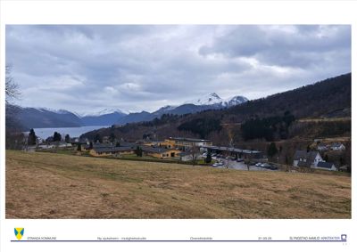 Fotografi av eksisterende bygninger i et landskap med fjell og vann i bakgrunnen.