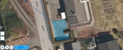 Satellittbilde (flyfoto) av et tomt med overlagte tegninger som viser eiendomsgrenser (røde linjer) og en planlagt bygning (blå polygon).