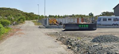 Fotografi av et utendørs område, sannsynligvis en byggeplass eller tomt, med en container, en campingvogn og en vei.