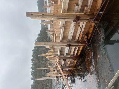 Fotografi av en byggeplass ved vannet, som viser et utstykkingssystem med trebjelker og stålstenger.