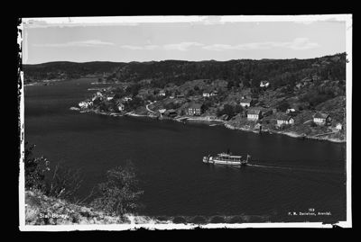 Et svart-hvitt fotografi som viser en kystbygd (Slåtterøy) med hus langs kysten, et vann og en båt.