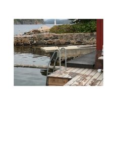 Fotografi av en uteplass med tredekk, steinmur og vann i bakgrunnen.