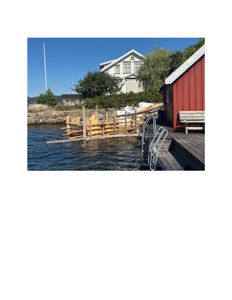 Fotografi av en bygning ved vannet med et utstyrt brygge i forgrunnen.