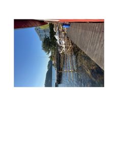 Fotografi av en byggeplass ved vannet med et tredekk, en rød konstruksjon i forgrunnen og en hvit bygning i bakgrunnen.