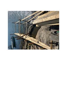 Fotografi av en utvendig konstruksjon, sannsynligvis et treplattformer eller en brygge som er under bygging ved kysten.