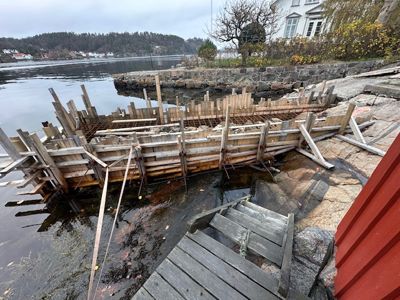 Fotografi av en byggeplass ved vannet, der det er satt opp betongformer (slikke) for å støpe et fundament eller en kai.