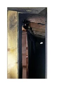 Fotografi av en åpen døråpning eller ramme, der man ser inn i et mørkt rom. Bildet viser detaljer i treverk og isolasjon.