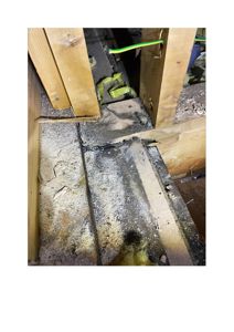 Fotografi av en konstruksjonsskade eller skade på et gulv/loft, der det er synlig råtne treverk, isolasjon og elektrisk ledning.