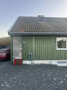 Fotografi av fasaden på en grønn, enetasjes bygning med tak, vinduer og en bil parkert ved siden av.