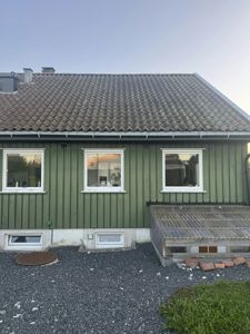 Fotografi av fasaden på en grønn farget, enetasjes bygning med tak av taktegl. Bildet viser vinduer, takrenne og en liten utbygging i høyre hjørne.