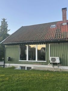 Fotografi av en grønn villa sett fra siden, med tak, vinduer og en luftkondisjonsenhet synlig.