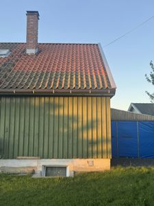 Fotografi av en grønnfarget bygning med rødt tak sett fra siden.