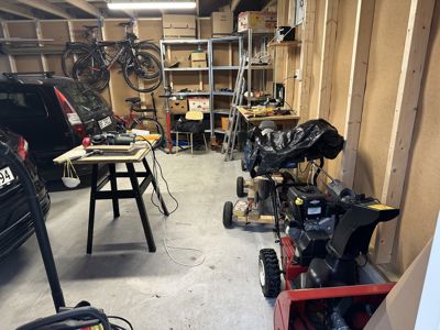 Fotografi av en garasje eller verksted med biler, sykler og verktøy.
