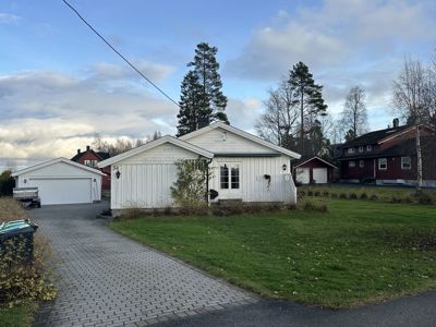 Fotografi av en hvit enebolig med kjeller, garasje og hage.