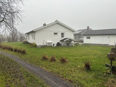 Fotografi av en hvit enebolig og en tilhørende bygning på en grønn tomt.