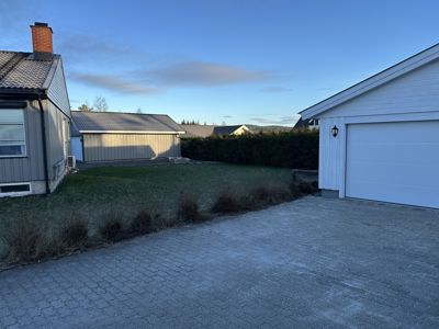 Fotografi av en bolig med garasje, hage og kjelinger.