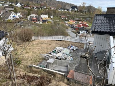 Fotografi av en bakgård med en terrasse, en hekk, og utsikt over nabolaget.
