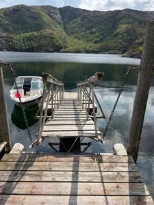 Fotografi av en brygge med en båt ved siden av, med fjell og vann i bakgrunnen.