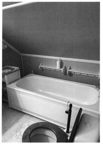 Sort-hvitt fotografi av et bad med badekar, toalett og veggmonterte hyller.