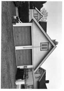 Sort-hvitt fotografi av en bolig med garasjeport sett fra siden.