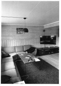 Sort-hvitt fotografi av et innendørs stueområde med sofa, TV og møbler.