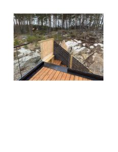 Fotografi av en utvendig trapp med glassrailing og tretrinn som fører nedover mot en steinete bakke i en skog.