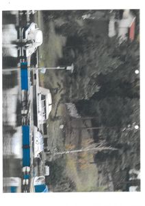 Fotografi av en utendørs scene med båter, en gate og trær.