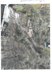 Fotografi av en bratt, skogkledt terreng med trapper og en bygning i bakgrunnen.