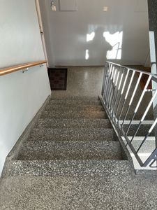 Fotografi av en trapp med terrazzo-trinn, håndtak og en dørmatte i gangen.