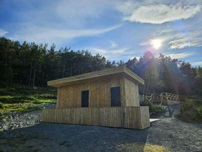 Fotografi av en ferdigbygd, liten trehytte eller utedo i en skogskant.