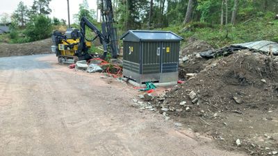 Fotografi av en byggeplass med en gjenstand som ser ut til å være en transformatorstasjon eller en lignende teknisk enhet, samt en graver.