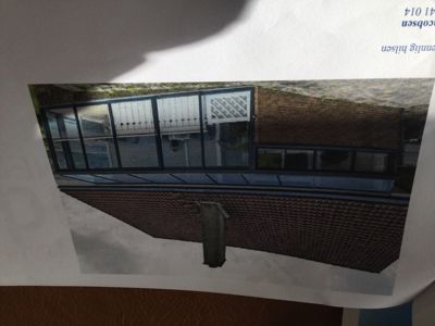 Fotografi av en bygning sett fra siden, som viser en ny tilbygget glassfasade og en eksisterende teglvegg.