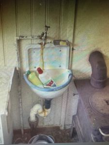 Fotografi av en gammel vaskebunn med kran og rør i et rom, sannsynligvis en kjeller eller utedo.