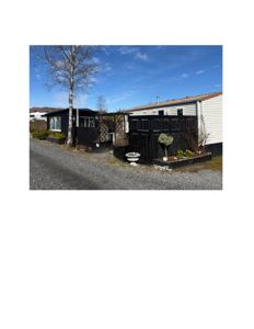 Fotografi av en bolig med en mørk utbygging eller uthus, sett fra en grusvei.